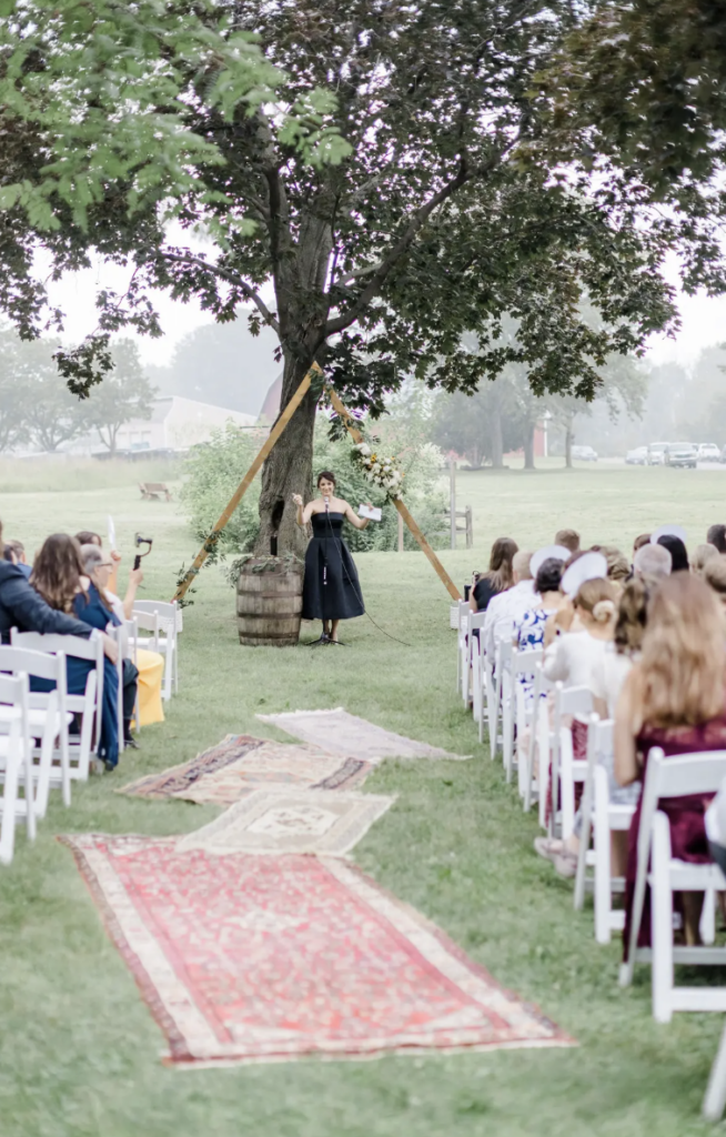 An outdoor ceremony at The Nature Place with white chairs and vintage rugs lining the isle.